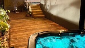En træterrasse med jacuzzi, lyskæder og en trappe, der fører til et overdækket område.