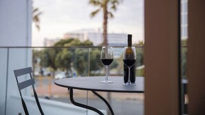 A table with two wine glasses and a bottle on a balcony with a view of palm trees and buildings. - Seaside 8: Stylish Seaside Studio with Balcony (Cape Town)