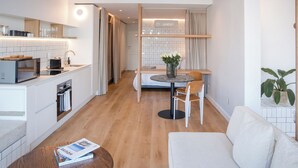 A modern kitchen with a dining area, a sofa, and a small table with a magazine. - Seaside 8: Stylish Seaside Studio with Balcony (Cape Town)