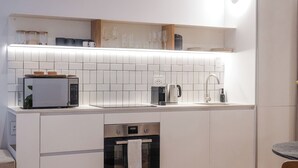 A modern kitchen with white cabinetry, a built-in microwave, a coffee maker, and a kettle. - Seaside 8: Stylish Seaside Studio with Balcony (Cape Town)