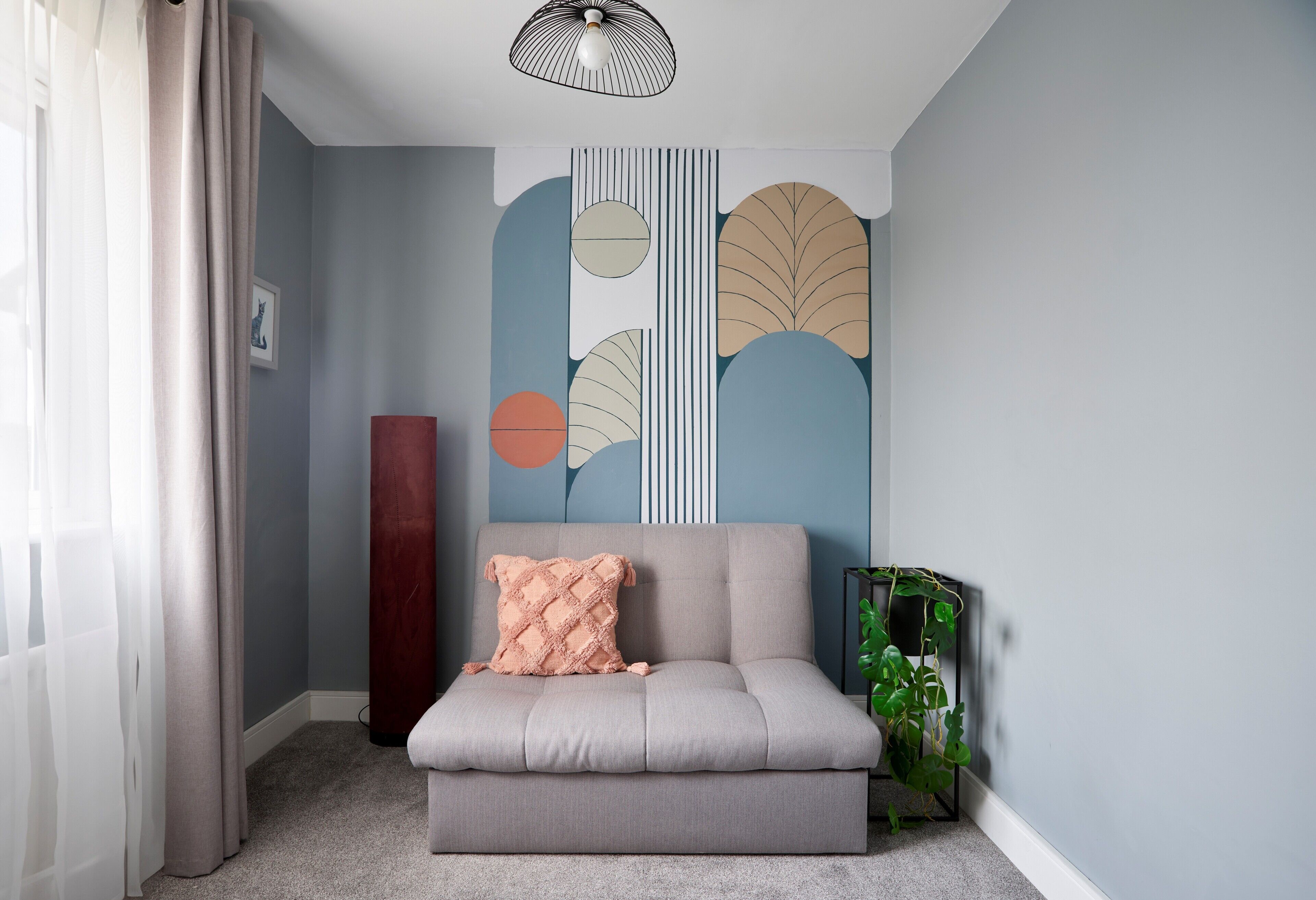 Un salon moderne avec un canapé gris, un mur décoratif orné de motifs abstraits, un pilier rouge imposant et une plante en pot.