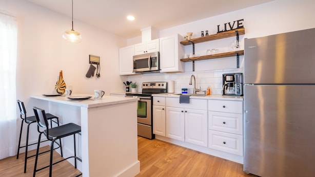 A modern kitchen with white cabinets, stainless steel appliances, a wooden island with bar stools, and a 'LIVE' sign on the wall. - Pet-Free Studio Rental on 2nd Floor w/ Parking (San Antonio)