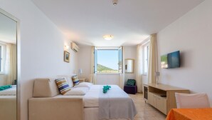 A hotel room with a bed, a sofa, a TV, a desk, and a window with a view of the beach. - Lovely apartment in Vinjerac (Vinjerac)