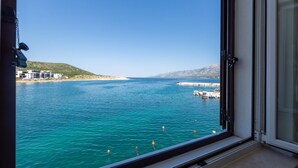 A coastal view from a window overlooking turquoise sea, buildings, and a hilly landscape. - Lovely apartment in Vinjerac (Vinjerac)