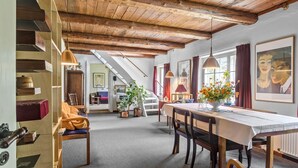 Un comedor acogedor con una mesa de madera, sillas y un jarrón de flores. Una escalera conduce a un nivel superior.