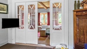 Una habitación con televisión, un armario de madera y una puerta que da a otra habitación con cama y ventana.