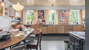 Una cocina moderna con armarios de madera, una isla central, iluminación colgante y ventanas grandes con cortinas.
