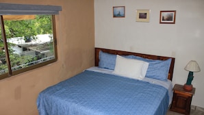 Un dormitorio con cama, ventana y mesita de noche con lámpara.