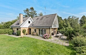 A two-story house with a sloped roof, a chimney, and a patio area with outdoor furniture. - Stunning home in Hundested with WiFi (Hundested)