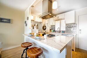 Une cuisine moderne dotée d’un îlot en marbre, de tabourets en bois et d’appareils électroménagers en acier inoxydable.