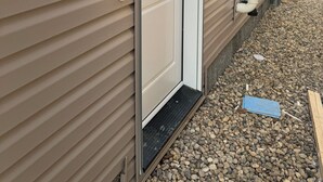 Un bâtiment à la façade beige, avec une porte blanche et un petit seuil menant à l’entrée.