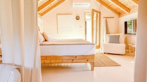 Une chambre avec un plafond en bois, un lit, une chaise blanche et une fenêtre.