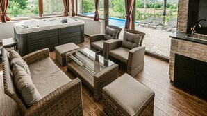 Una zona exterior moderna amb mobiliari de vimet, una taula de cafè amb tapa de vidre i una banyera hidromassatge.