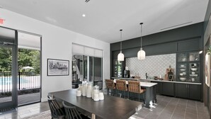 Een moderne keuken met donkere kastjes, een centraal eiland, hanglampen en een eethoek met stoelen.