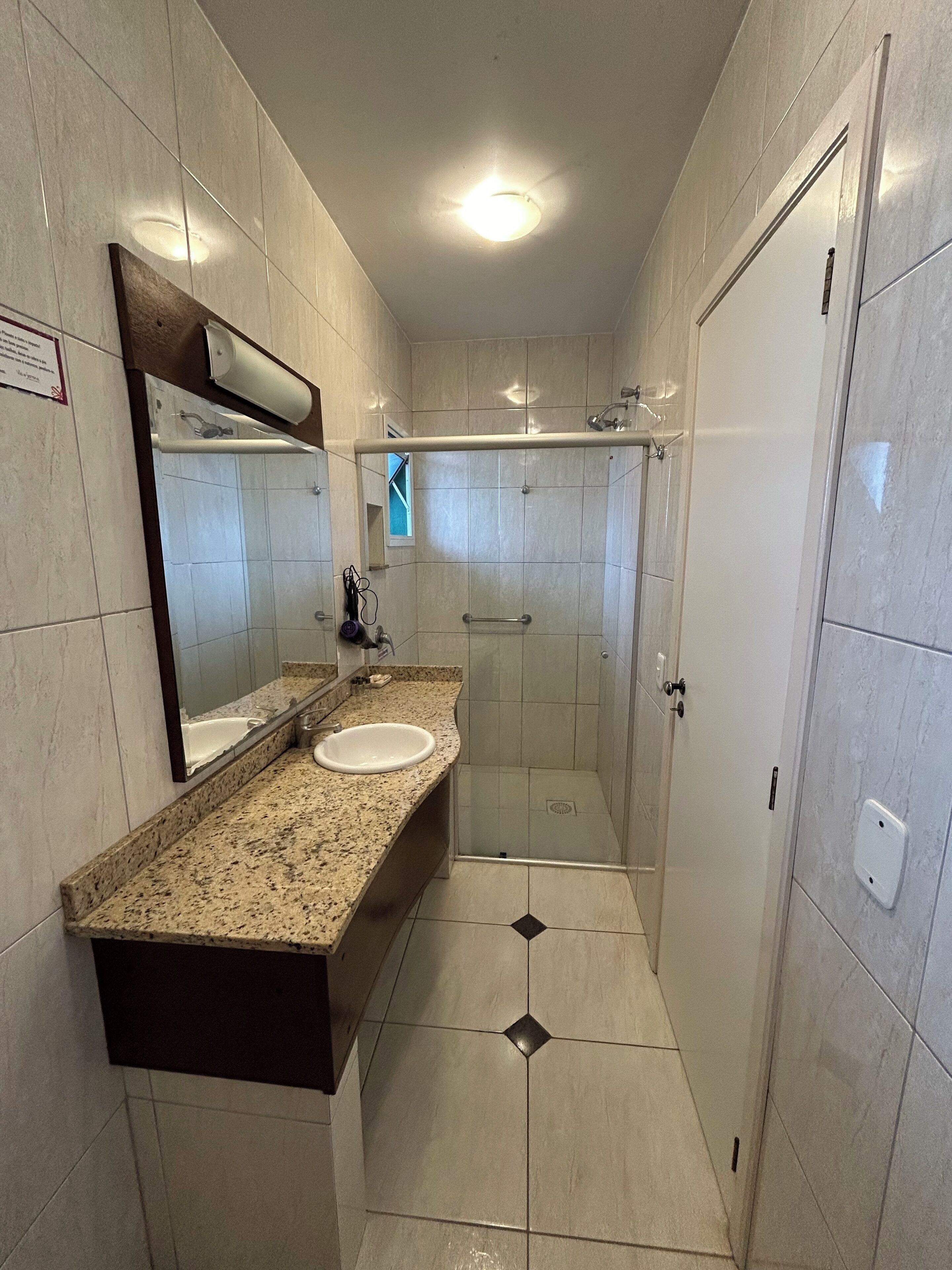 A bathroom with a granite countertop, a sink, a mirror, a shower with a glass door, and tiled walls.