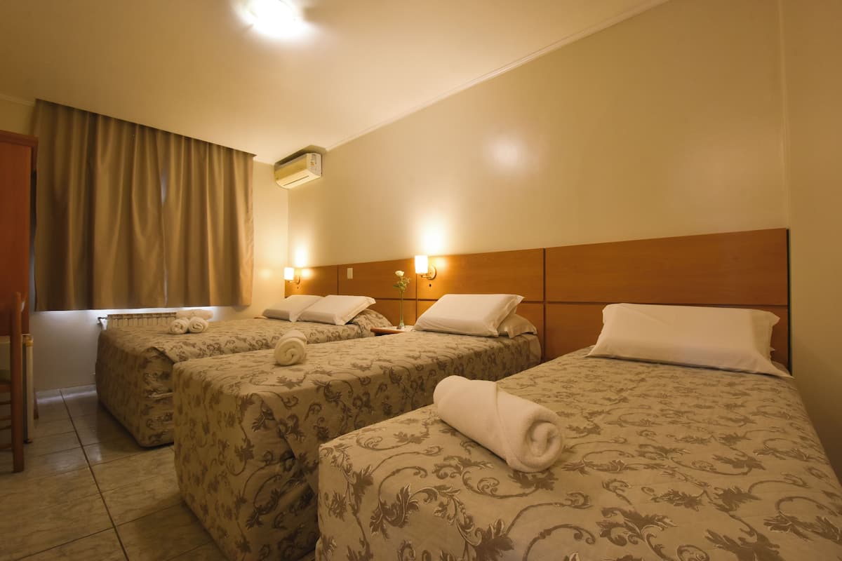 A hotel room with three beds, each with a floral-patterned bedspread and neatly folded towels.