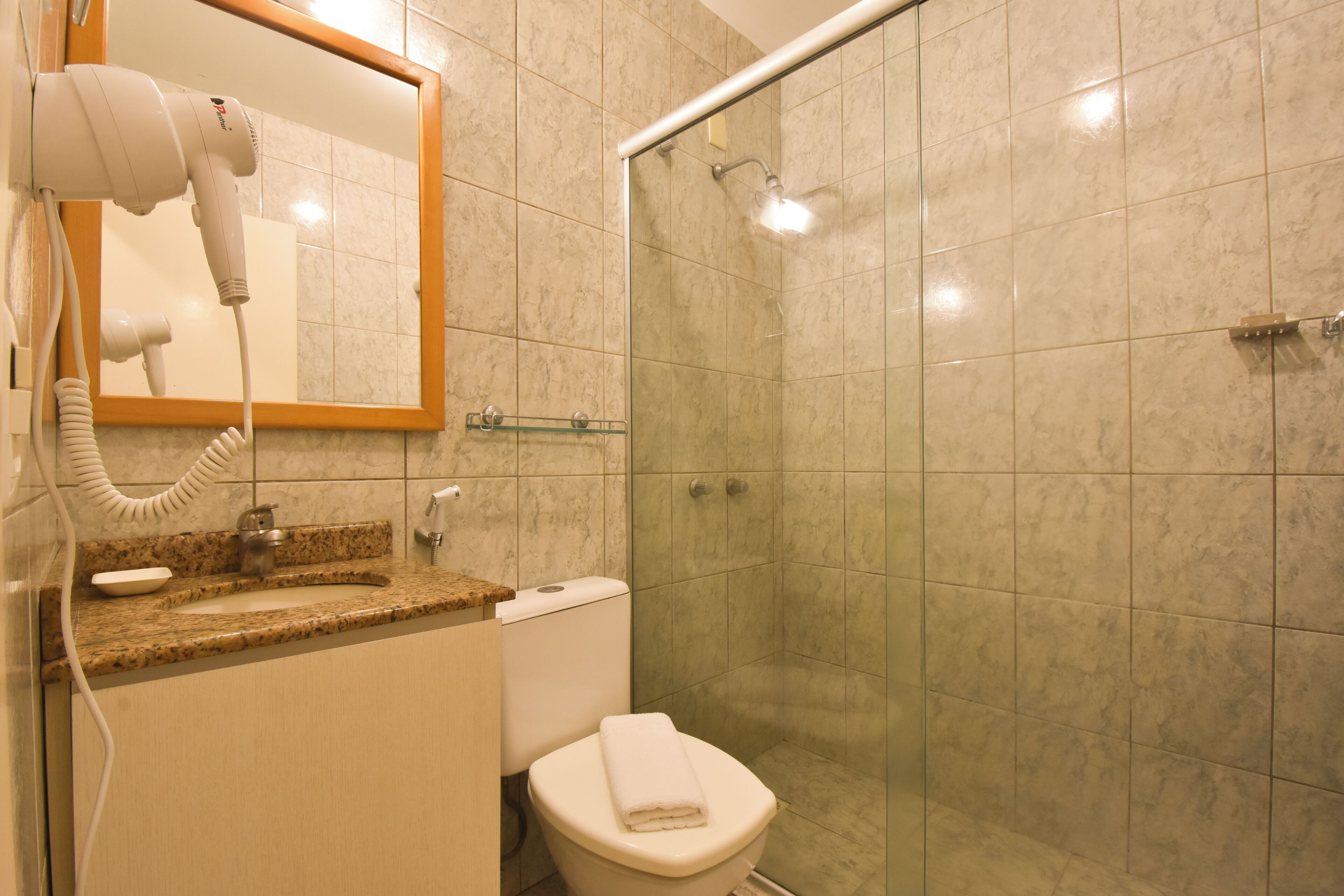 A bathroom with a hairdryer, sink, toilet, and a glass shower enclosure.