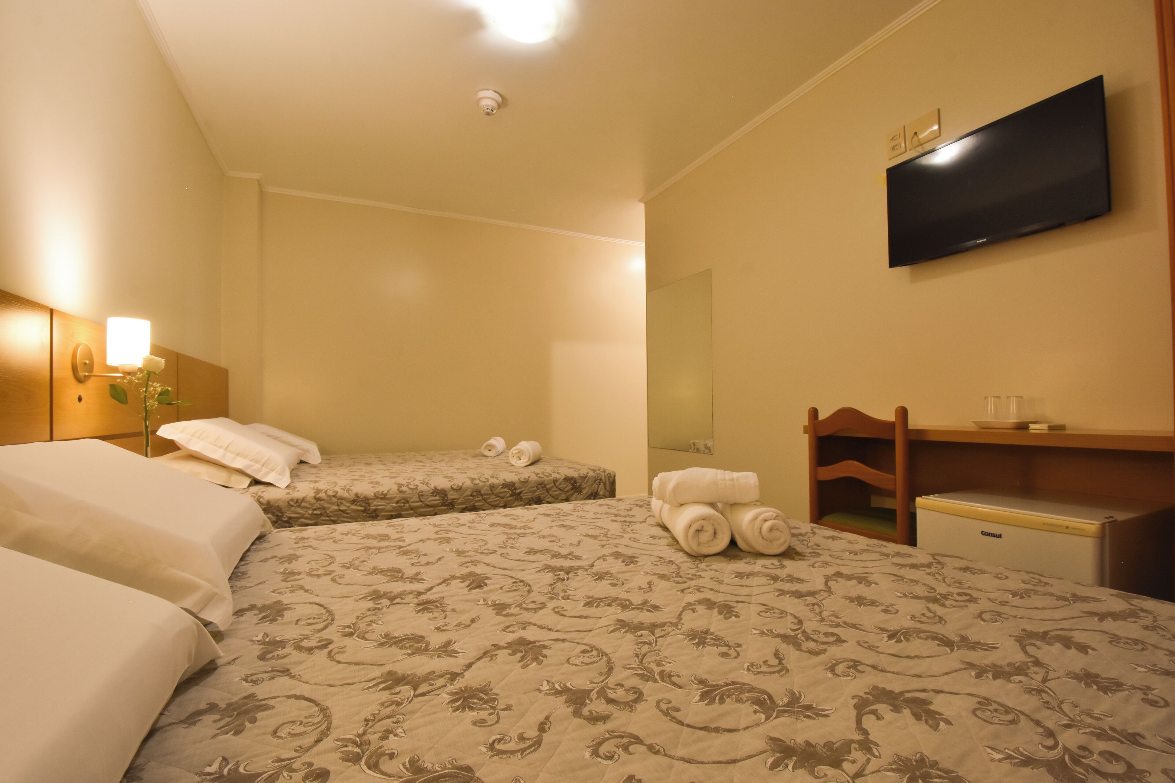 Une chambre d’hôtel avec deux lits, un téléviseur à écran plat, un minibar et une tête de lit en bois.