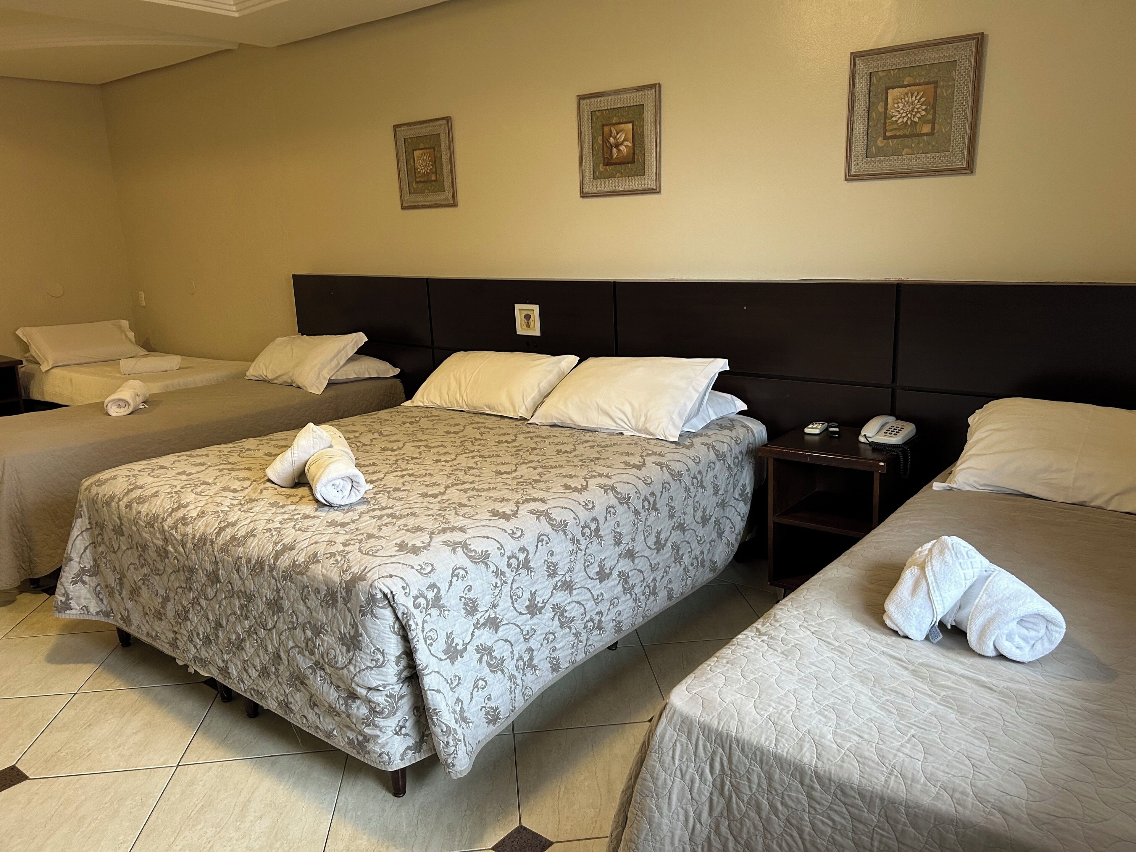 A hotel room with two single beds, a double bed, and a nightstand with a phone.