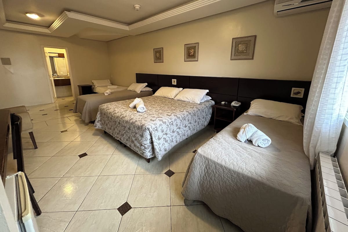 A hotel room with two beds, a desk, a chair, a small table, and a bathroom visible through an open door.