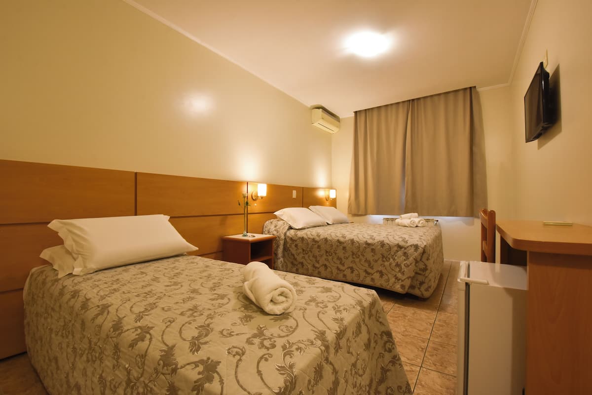 A hotel room with two beds, a desk, a TV, and a window with curtains.