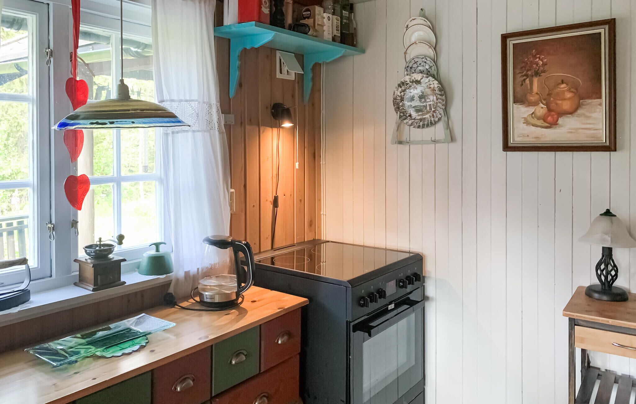 Une cuisine équipée d’une cuisinière, d’une bouilloire et d’une fenêtre avec des rideaux.
