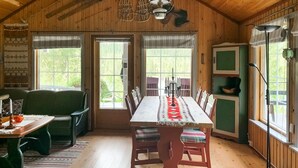 Un acogedor interior de cabaña con una mesa de comedor, sillas, un sofá y un ventanal grande.