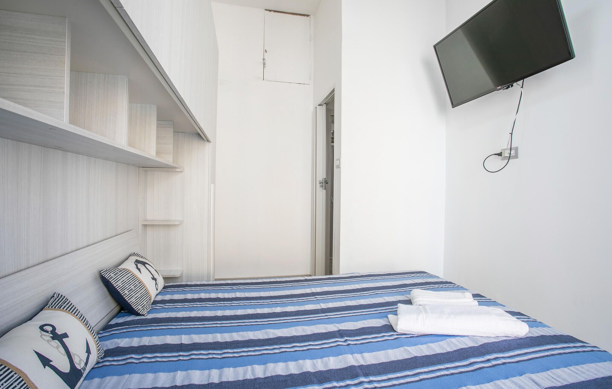 A bedroom with a bed, a TV, and a door leading to another room.