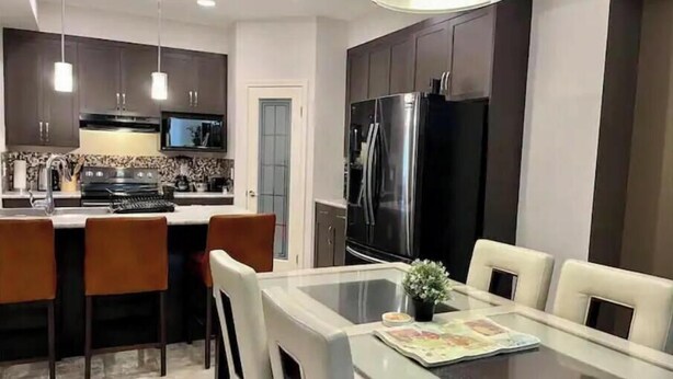 Una cocina moderna con armarios oscuros, electrodomésticos de acero inoxidable y una mesa de comedor de vidrio con sillas.