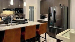 Una cocina moderna con armarios oscuros, electrodomésticos de acero inoxidable e iluminación colgante.