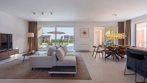 A modern living room with a sofa, TV, and dining area with a view of the outdoors.