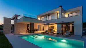 A modern two-story house with a swimming pool, outdoor seating, and a well-lit patio area.
