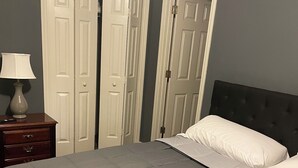 A bedroom with a bed, a nightstand, and two open doors leading to other rooms. - Genroc-"It's your home too" (Tallahassee)