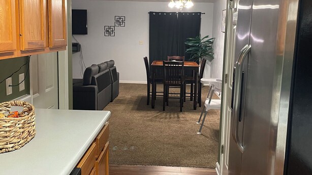 A kitchen with wooden cabinets, a stainless steel refrigerator, and a dining area with a table and chairs. - Genroc-"It's your home too" (Tallahassee)