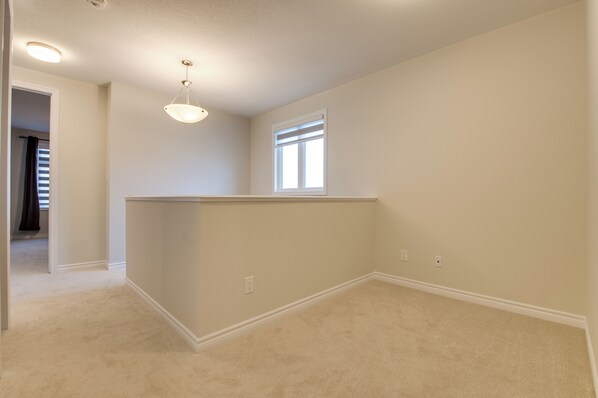 A spacious, carpeted room with a large window, a ceiling light fixture, and a door leading to another area.