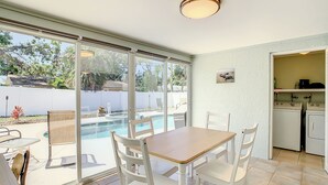 A room with a dining table and chairs, a view of a swimming pool, and a laundry area with washing machines.