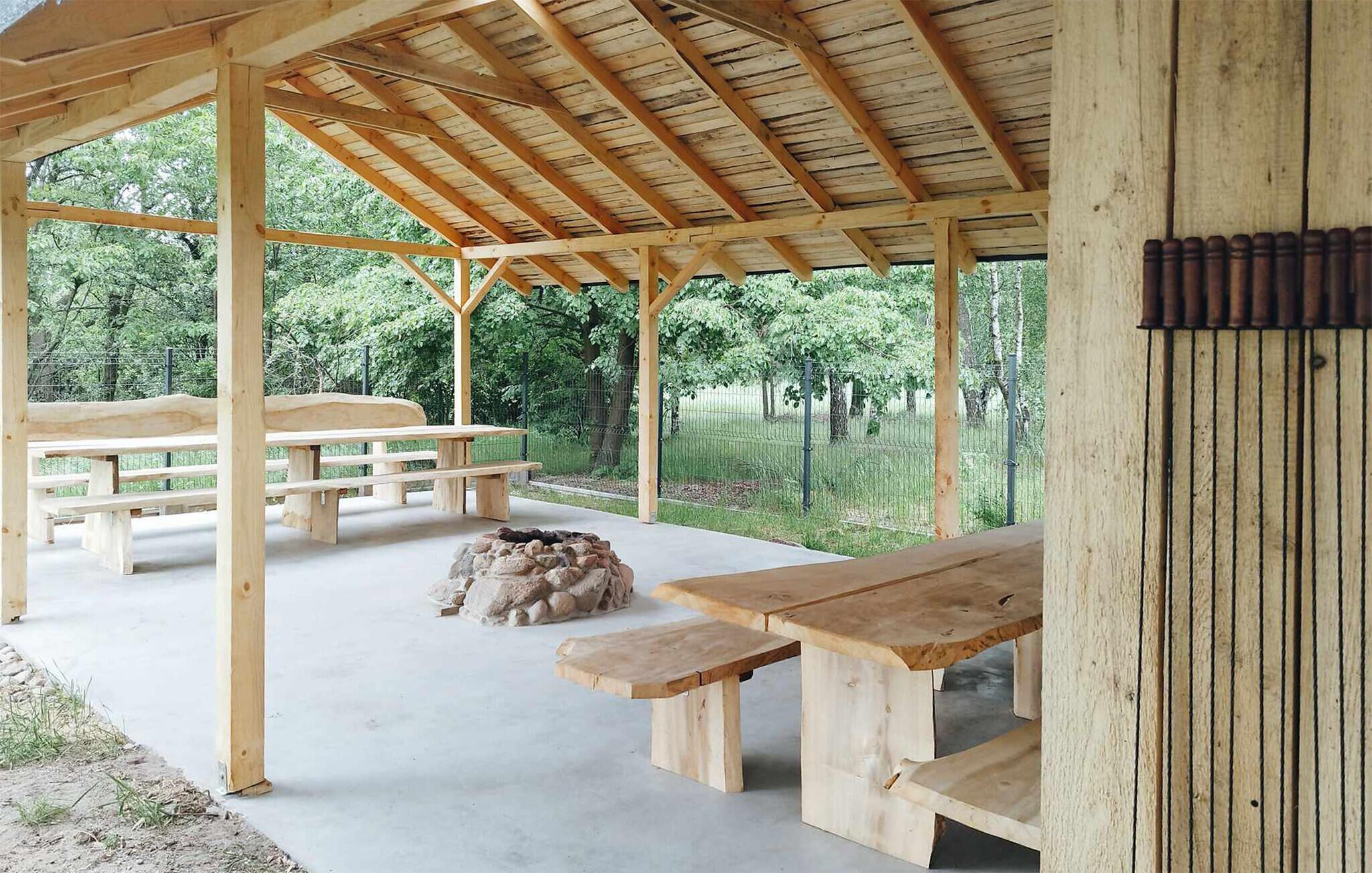 A covered outdoor area with wooden picnic tables and benches, surrounded by a fence and trees.