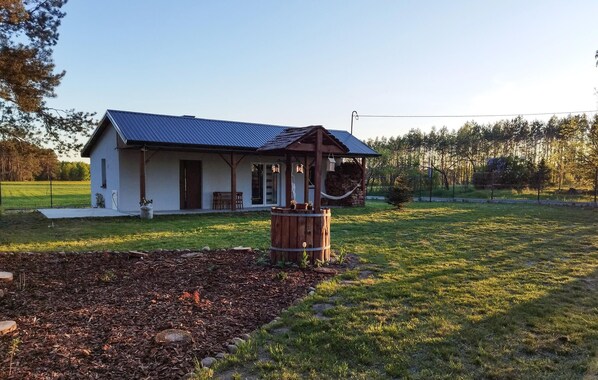 Une maison de plain-pied avec un toit bleu, une véranda et un tonneau en bois dans la cour.