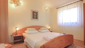 Un dormitorio ordenado con una cama de madera, lámparas de noche, una mesita y una ventana con cortinas.
