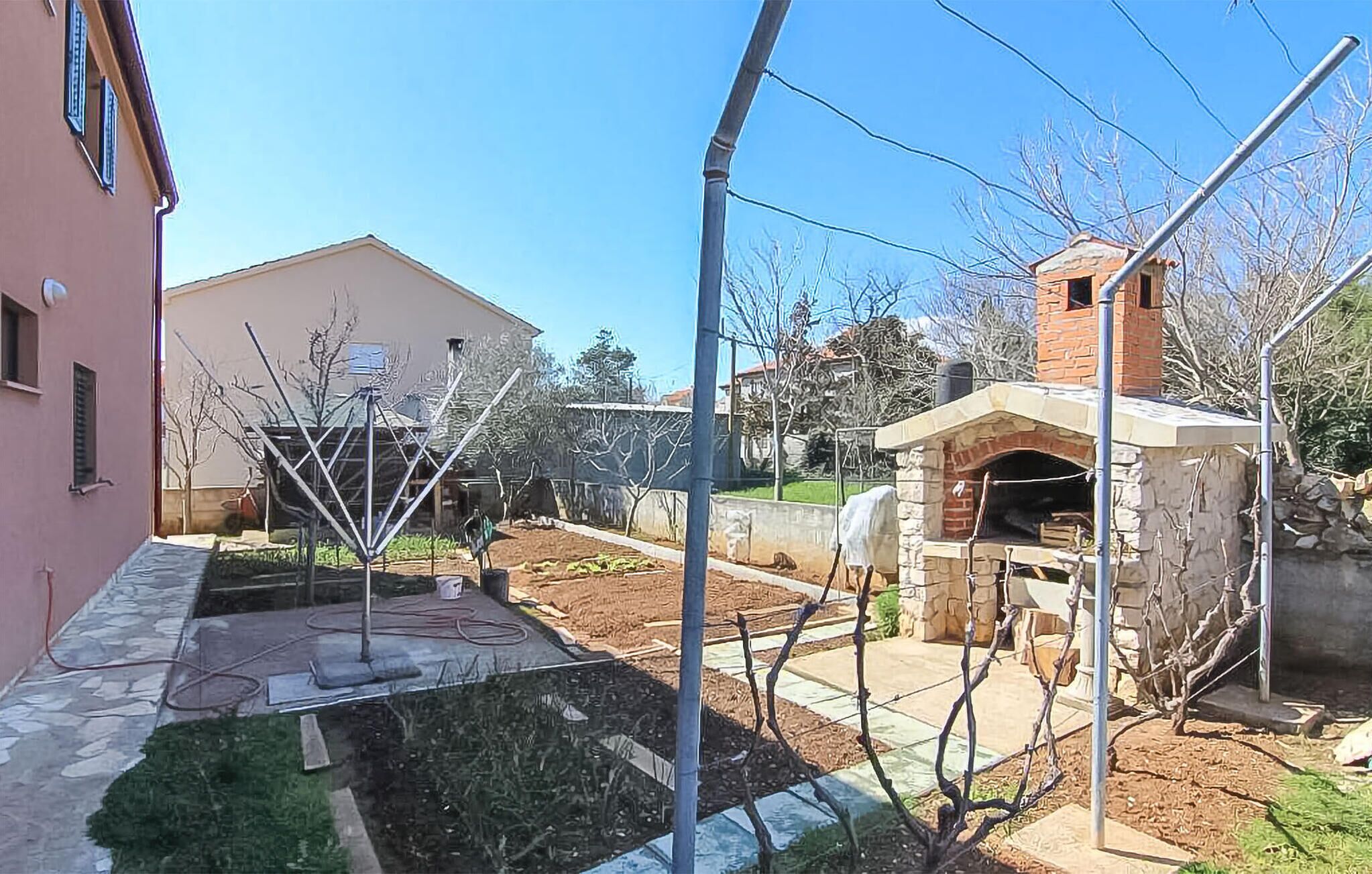 Une cour avec un four extérieur en pierre, une structure métallique et un bâtiment rose.