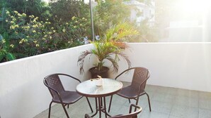 Una mesa redonda con cuatro sillas de mimbre en un balcón con pared blanca y plantas en macetas.