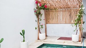Un área de piscina con una pérgola de bambú, plantas en macetas y una piscina cristalina.