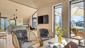 Et moderne interiør med fletningsmøbler, et spisebord og et fjernsyn monteret på væggen.