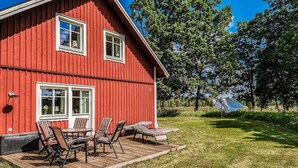 Una casa de madera roja con terraza, mobiliario exterior y vistas a árboles y al cielo.