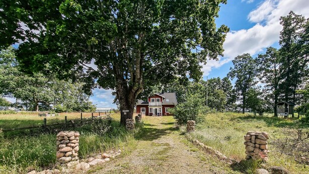 Una casa roja con estructura de dos pisos, rodeada de árboles y un camino de piedra.
