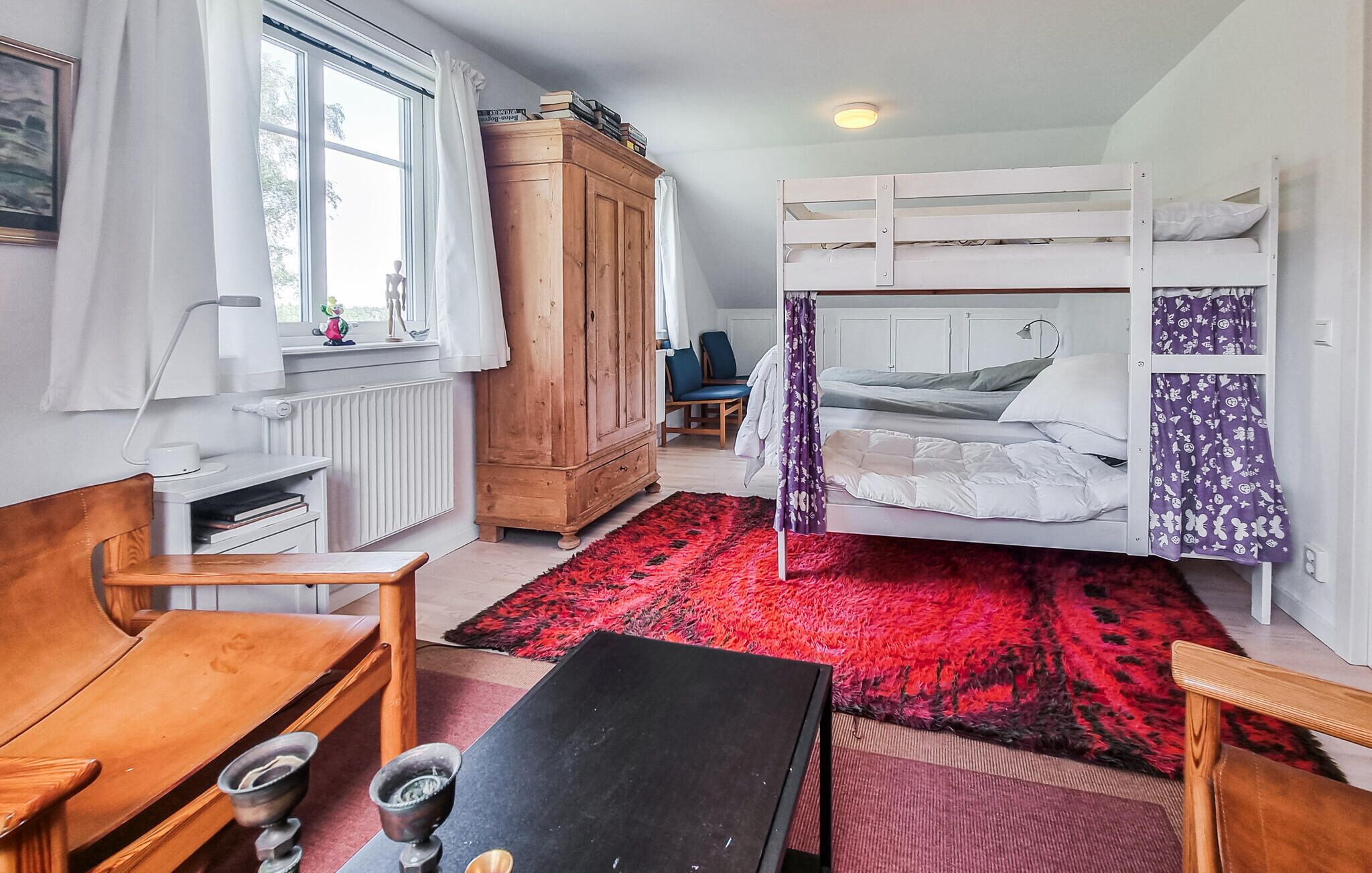 Una camera compatta con un letto a castello, un armadietto in legno, una scrivania e una finestra con tende.