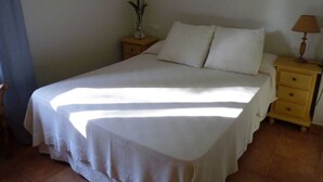 Una cama bien hecha con ropa blanca, una mesita de noche con una lámpara y un florero con flores en la mesita de noche.
