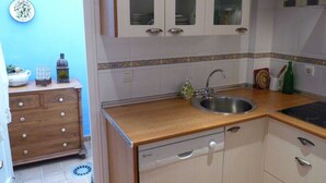 Una cocina compacta con lavavajillas, un fregadero y un armario con puertas de vidrio.