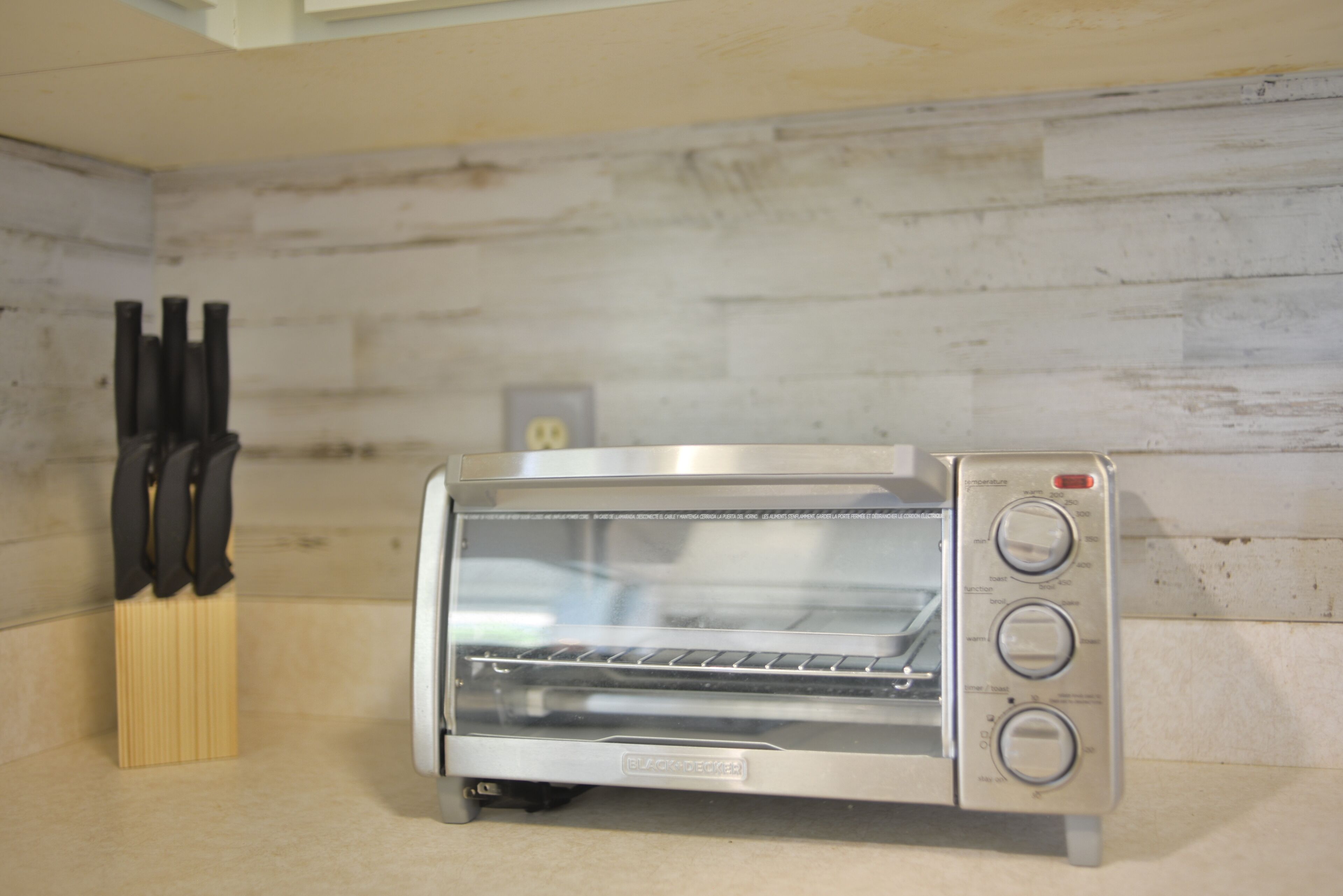 A kitchen with a toaster oven, a knife block, and a wooden backsplash.