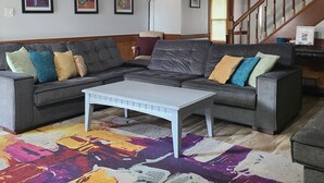 A living room with a sectional sofa, a coffee table, a colorful rug, and a staircase with wooden railings. - Vacation home just 21 minutes from Historic Beale Street and Graceland (Memphis)